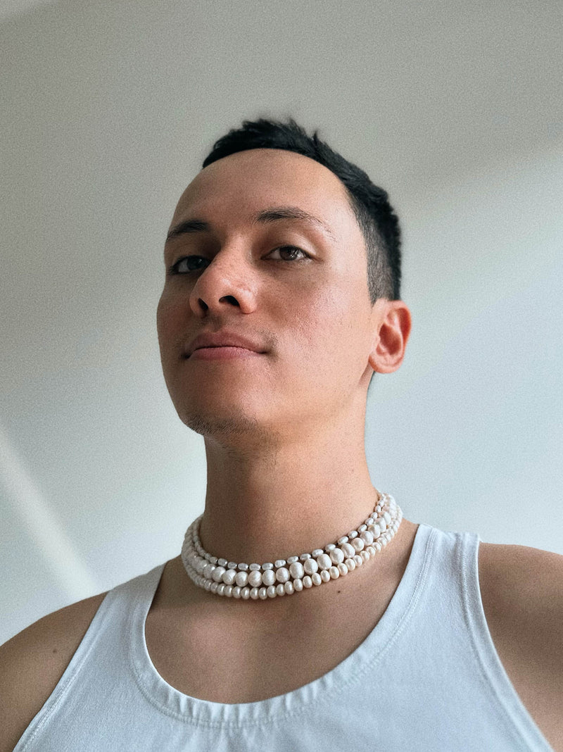 Male wearing a white tank top and multiple Pryte tide collections fresh water pearl necklaces against a plain background
