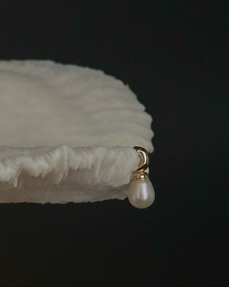 Pryte Medium Pearl Drop Earrings hanging on a coral setting on a dark background