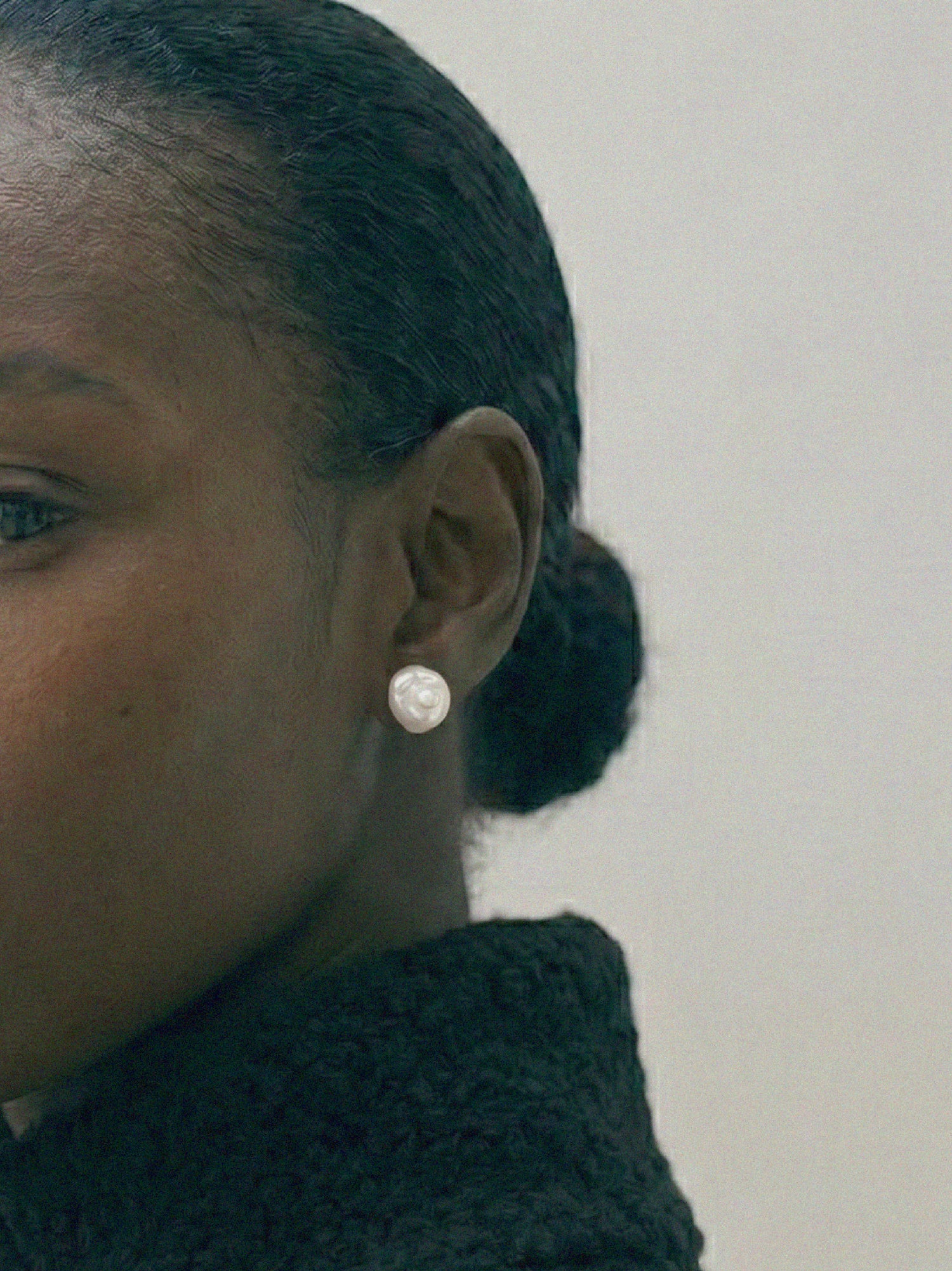 Close-up of a person wearing pryte baroque shell pearl ear studs against a neutral background